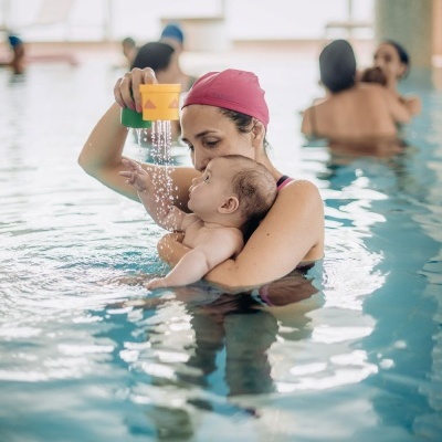 Mulher na piscina a segurar bebé com copos de plástico a verter água