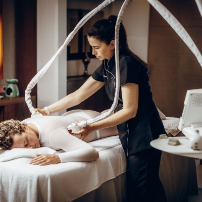 Tratamento de estética com máquina branca aplicada nas costas de mulher numa cama de massagem.