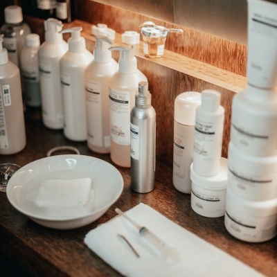 Produtos cosméticos em frascos e potes brancos e metálicos sobre superfície de madeira com pano branco e tigela