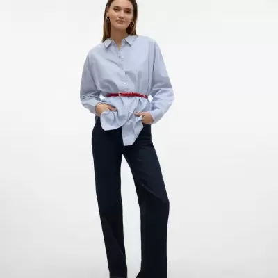 Mulher com camisa azul clara, cinto vermelho, calças de ganga azul escuro e sapatos pretos
