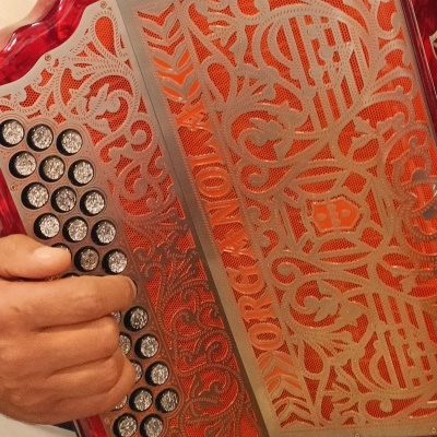 Acordeão vermelho com detalhes metálicos e botões em destaque, sendo tocado por uma pessoa