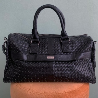 Mala de mão preta trançada com etiqueta AUGUSTA sobre superfície laranja