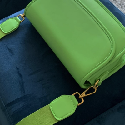 Bolsa verde com alça larga de tecido e detalhes dourados sobre superfície azul escura