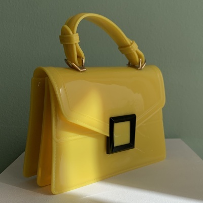Mala amarela de verniz com fivela preta e alça num fundo verde