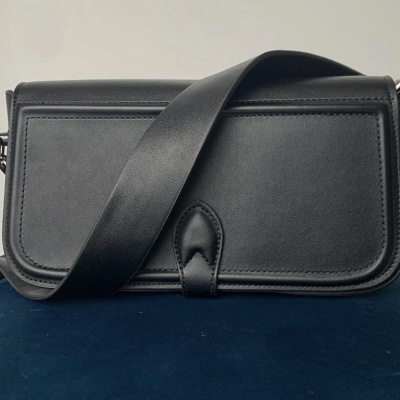 Mala preta rectangular com tira larga em couro liso sobre almofada azul