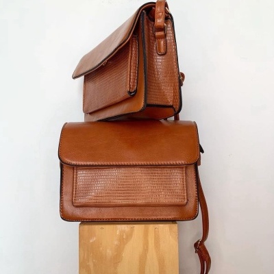 Duas malas castanhas de couro com textura granulada sobre suporte de madeira