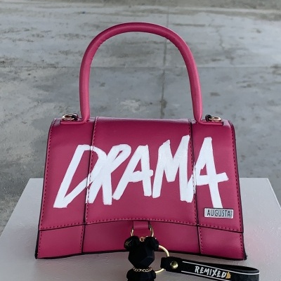 Mala de mão rosa com texto DRAMA e chaveiro preto