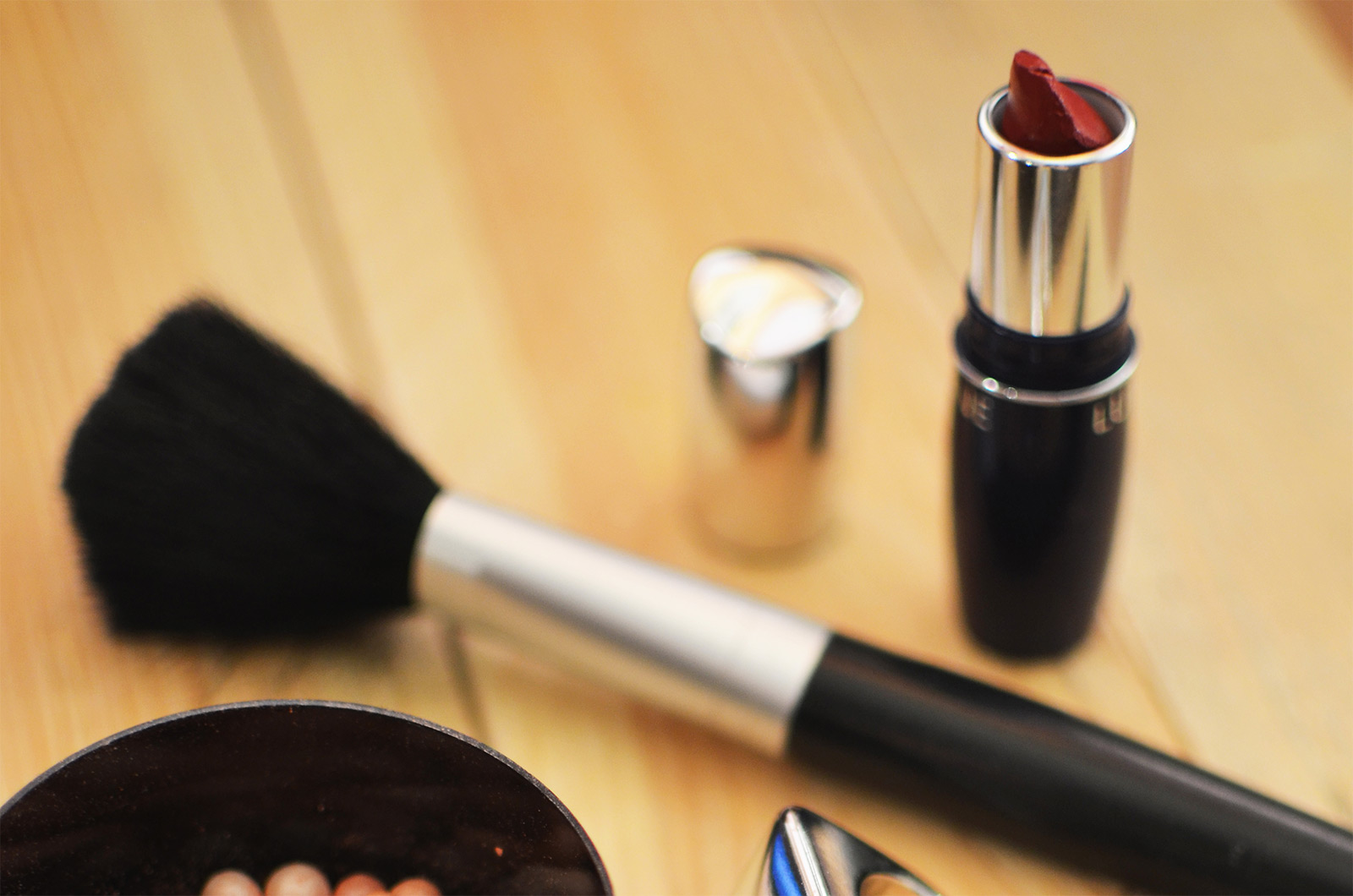batom vermelho, pincel de maquilhagem e tigela com esferas sobre mesa de madeira