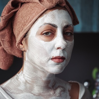 Mulher com máscara facial branca e toalha na cabeça
