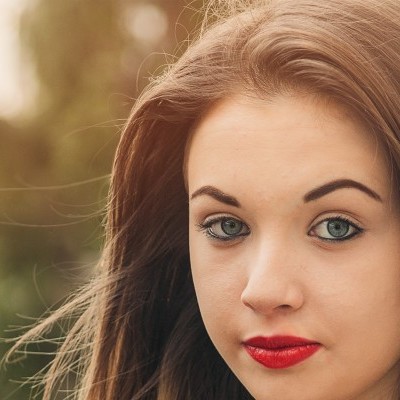 Retrato de jovem com cabelo castanho e batom vermelho ao ar livre