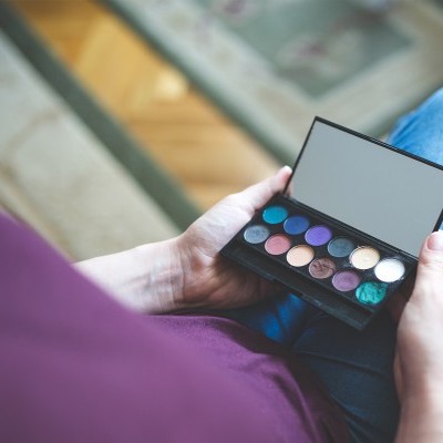 Paleta de sombras coloridas com espelho segurada por pessoa sentada