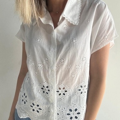 Blusa branca bordada com padrão floral e botão frontal, usada com calças jeans azuis.