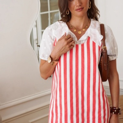 Vestido riscado branco e vermelho com blusa branca de bolinhas e folhos, acessórios dourados e mala castanha.