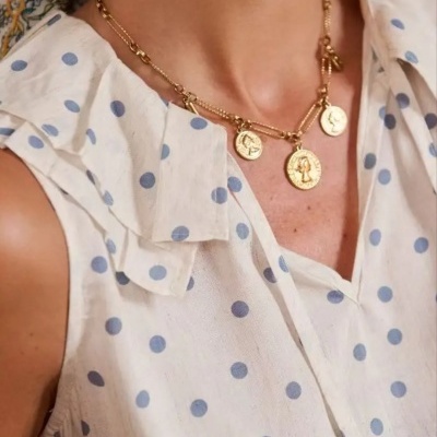 Mulher com blusa branca de bolinhas azuis e colar dourado com pendentes.