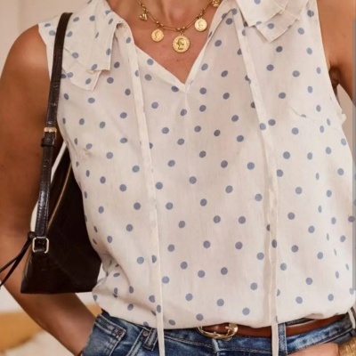 Top feminino branco com bolas azuis e gola com folhos, jeans azul e acessórios dourados