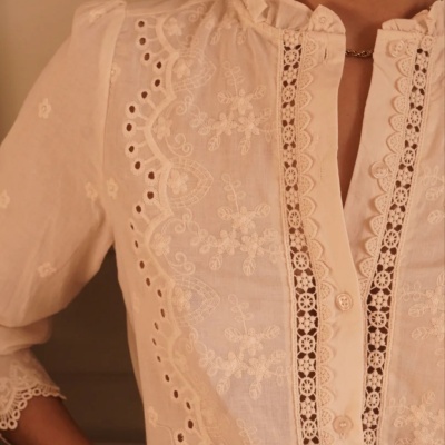 Blusa branca com bordados florais, detalhes em renda, botões frontais e gola franzida.