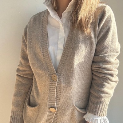 Cardigã bege claro de malha com botões e bolsos, sobre camisa branca com folhos na gola e punhos.