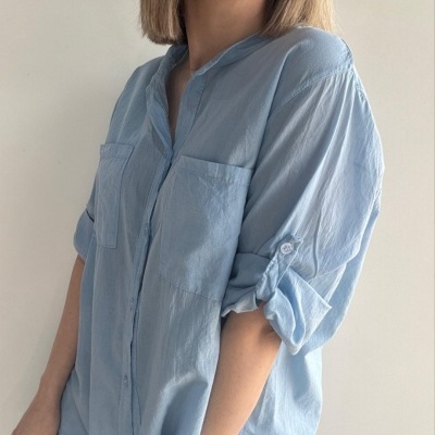 Camisa azul clara de tecido leve com bolsos frontais e mangas arregaçadas