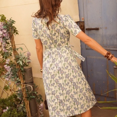 Vestido floral branco com sandálias cinza, vista de costas, em ambiente exterior com plantas e porta azul.