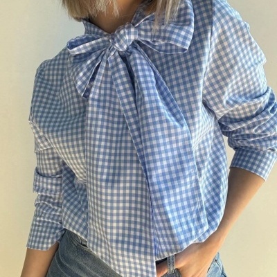 Camisa vichy azul claro e branco com gravata no pescoço e mangas compridas.