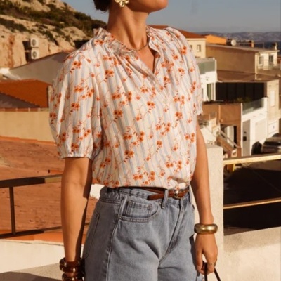 Mulher com blusa branca estampada, calções de ganga, acessórios dourados e óculos escuros