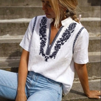 Blusa branca com bordados pretos e calças de ganga claras sentada nas escadas