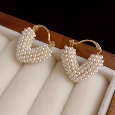 Brincos dourados com pérolas pequenas em formato de V numa caixa de veludo branco e madeira
