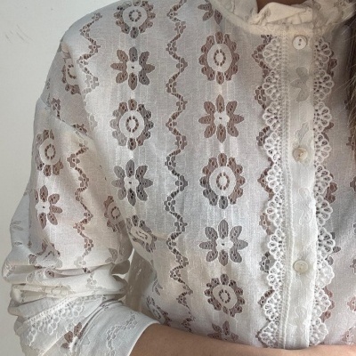 Blusa branca rendada com padrão floral e gola alta com babados