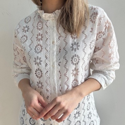 Blusa branca feminina com padrão floral e renda, botões e gola alta franzida.
