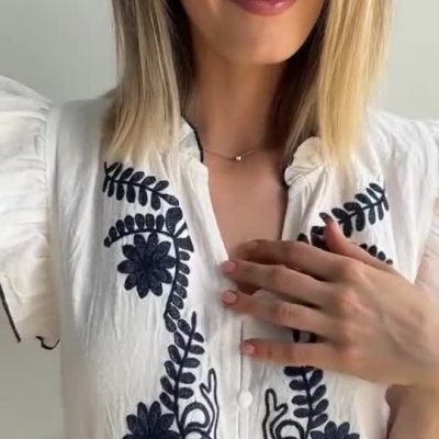 Mulher a usar blusa branca bordada com flores negras e jeans.