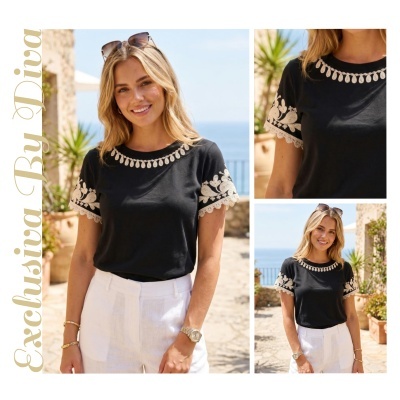 T-shirt preta com bordados brancos nas mangas e decote redondo, usada por mulher loira em ambiente exterior com vista para o mar