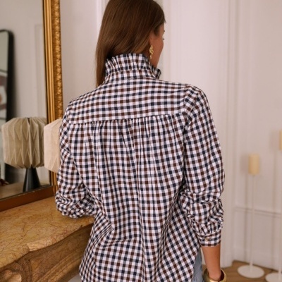 Blusa de manga comprida xadrez azul, branco e castanho vista de costas, com calças de ganga azuis e pulseira dourada em ambiente interior