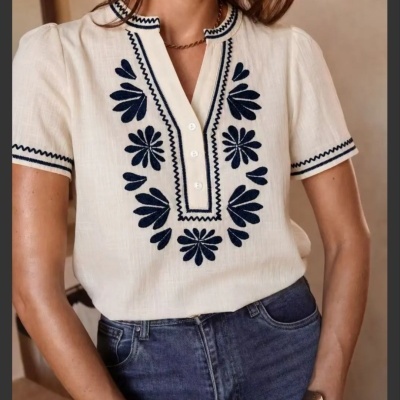 Blusa feminina creme com bordados florais azuis e botões, usada com jeans e acessórios.