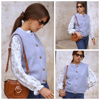 Mulher com camisola de malha azul clara, blusa branca com padrão cinza, calças azuis e mala castanha de couro