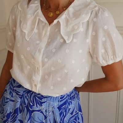 Blusa branca de bolinhas com gola ondulada e saia azul com padrão floral
