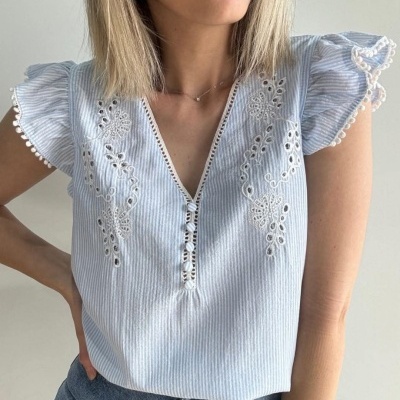 Blusa azul claro com bordados florais e botões, mangas curtas com bainha decorativa.