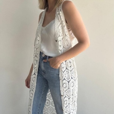 Mulher com colete de crochê branco, top branco e jeans azul