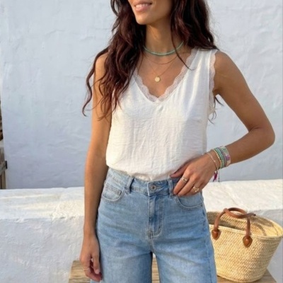 Mulher com camisola branca de renda e calções de ganga azuis posando com fundo branco e mala de palha