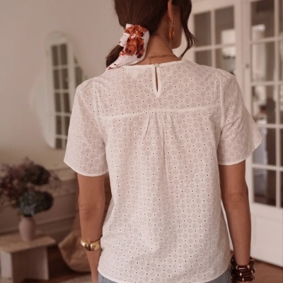 Blusa branca feminina com padrão de pequenos furos mostrada pelas costas.