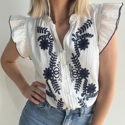 Blusa branca com bordados florais pretos e mangas com babados, usada com jeans azul claro.