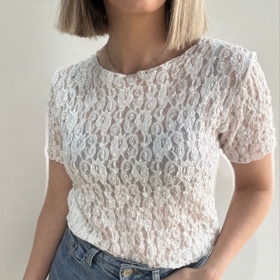 T-shirt branca em renda floral com mangas curtas e jeans azuis.
