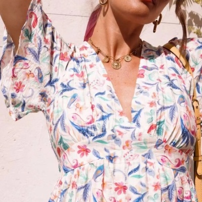 Vestido floral colorido branco de tecido leve com decote V e mangas curtas usado com óculos amarelos e colar dourado