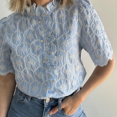 Camisa azul clara bordada com mangas curtas e botões, combinada com calças de ganga azuis.
