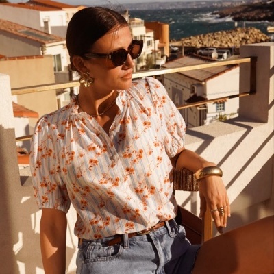 Mulher com blusa floral e calções de ganga numa varanda ao sol