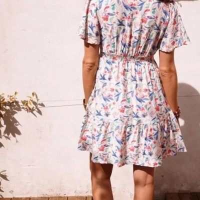 Vestido curto floral branco com sandálias brancas e lenço rosa no cabelo visto de costas
