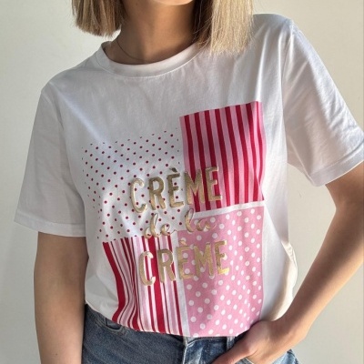 T-shirt branca com padrões rosa e vermelhos e texto dourado, usada com jeans azuis
