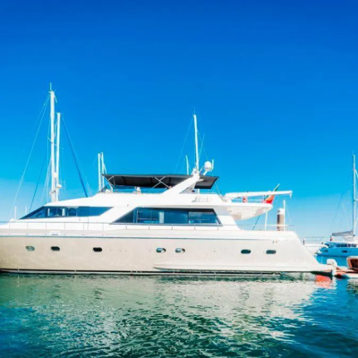 Iate branco ancorado numa marina com vários barcos à vela ao fundo