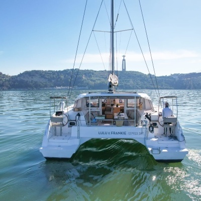 Catamaran branco na água com nome 'LU LU FERANDEZ' visível e homem sentado no convés.