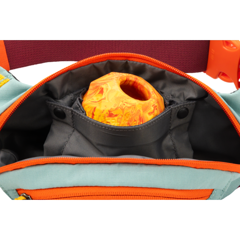 HOME TRAIL™ HIP PACK - River Rock Green - Ruffwear Mochila azul claro com detalhe laranja aberta mostrando bola laranja marmoreada dentro de bolso cinzento.