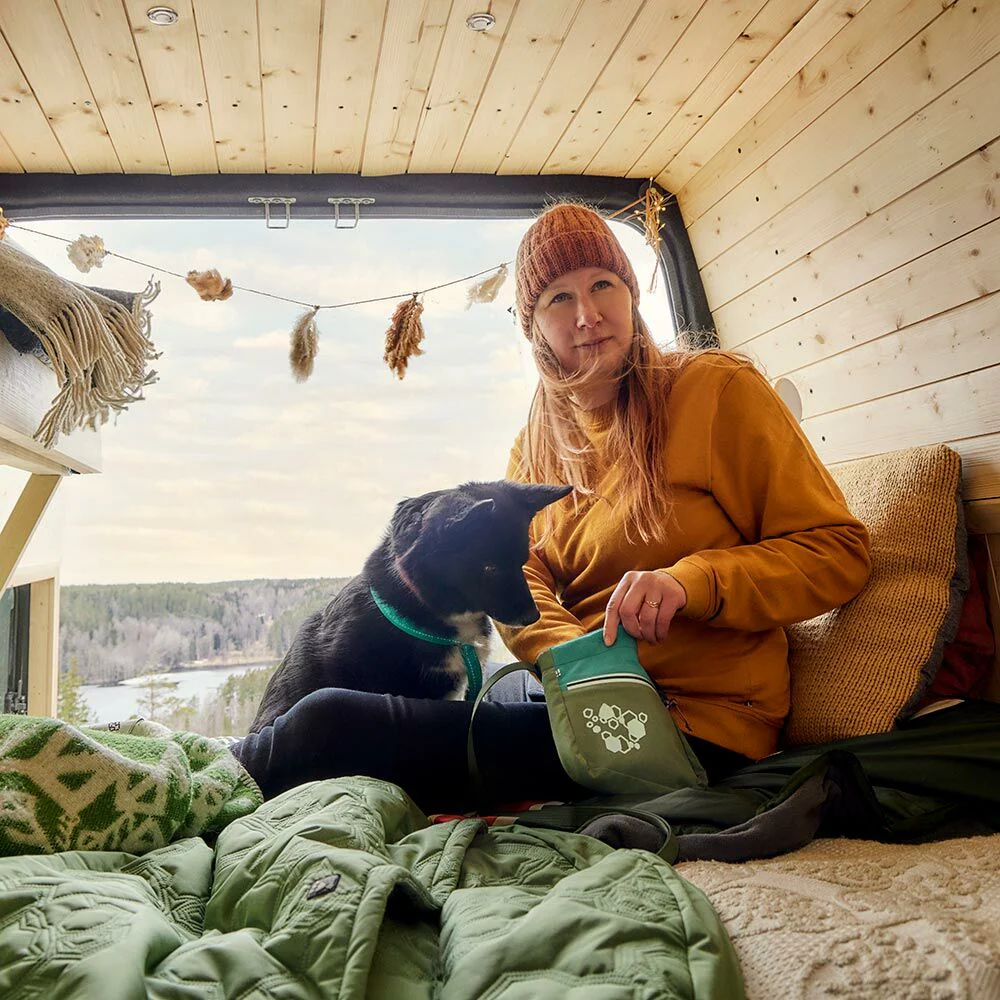 Treat Pocket ECO - Hurtta - Verde Mulher com cão numa cama com painéis de madeira e mantas verdes